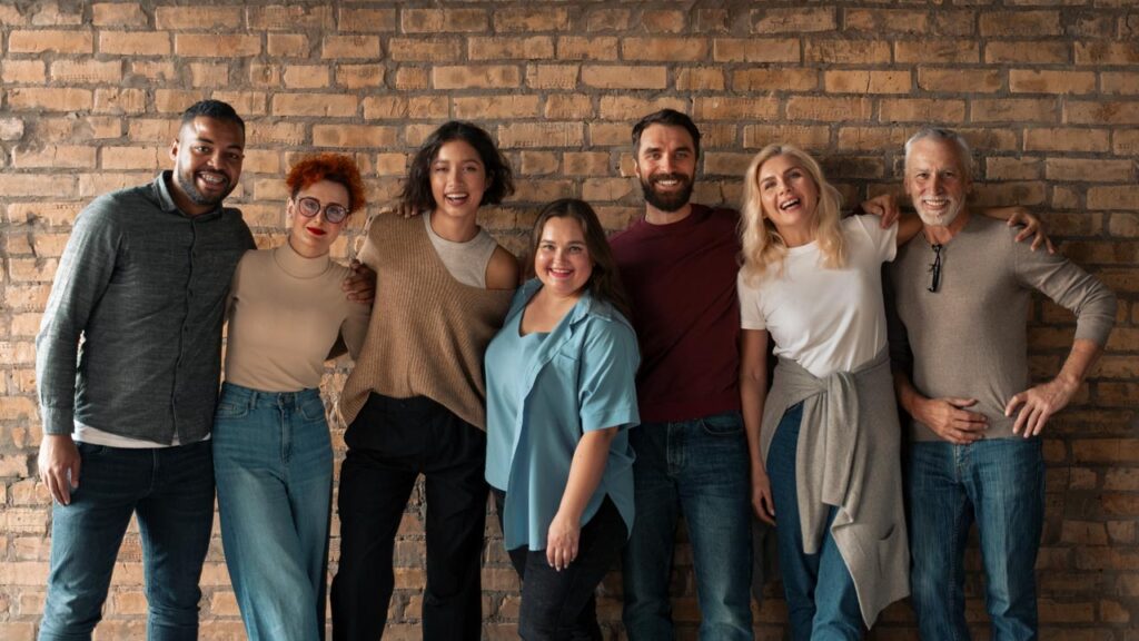 A group of seven people standing side by side, smiling in front of a brick wall.