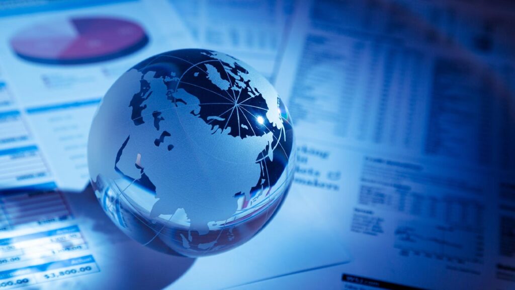 Glass globe with a map of Asia and Europe rests on financial documents, illuminated by blue light.